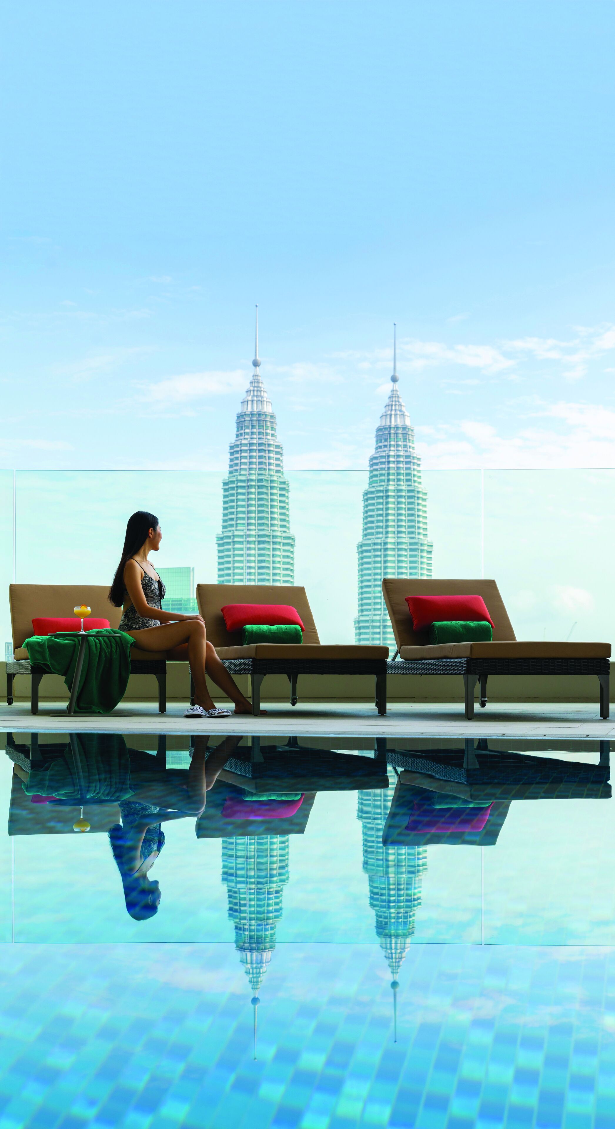 A person relaxing by a pool with a view of the Petronas Towers.