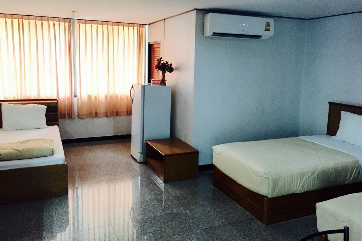 Een hotelkamer met twee bedden, een koelkast, een airconditioning en een raam met gordijnen.