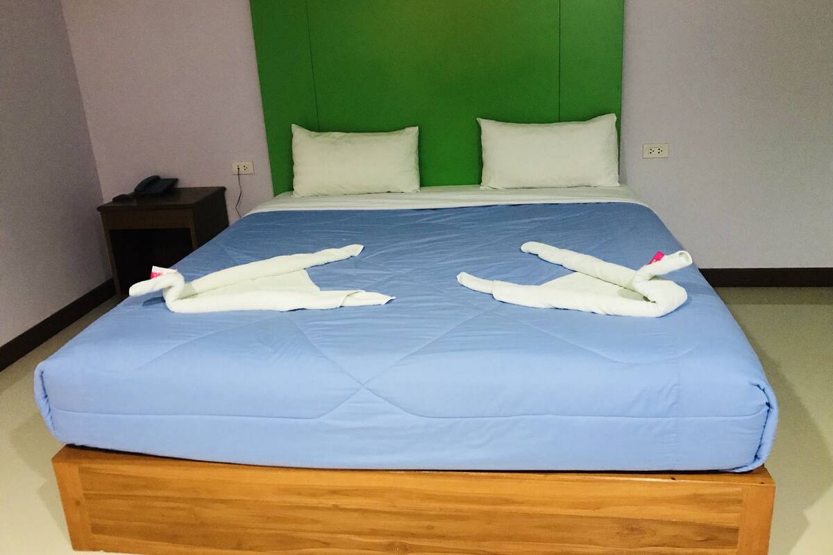 Een hotelkamer met een bed, twee kussens, een nachtkastje en twee handdoeken op het bed.