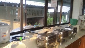 Een buffetopstelling met diverse voedseldispensers, een koffiezetapparaat en uitzicht op het buitenlandschap.