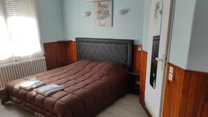 A bedroom with a brown quilted bed, a radiator, a wooden headboard, and a wall-mounted picture. - Hôtel de la place (Germigny-des-Pres)