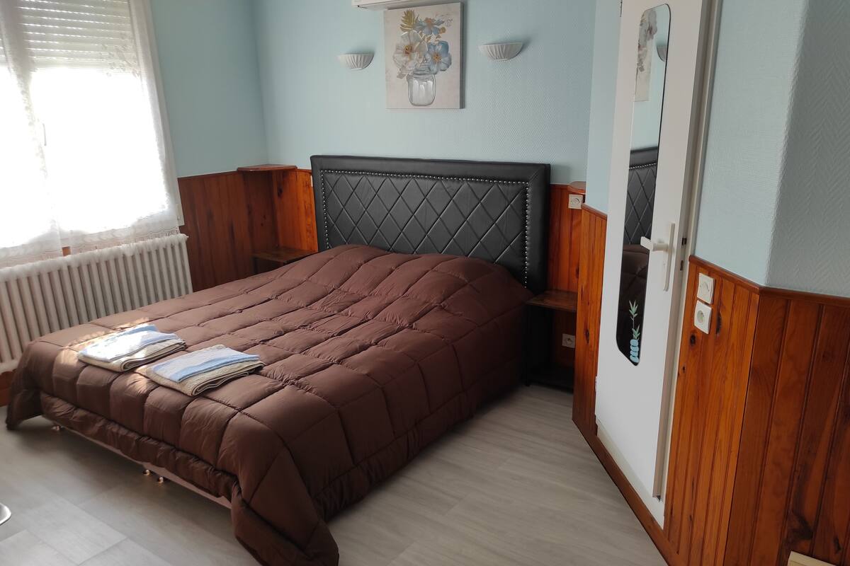 A bedroom with a brown quilted bed, a radiator, a wooden headboard, and a wall-mounted picture.