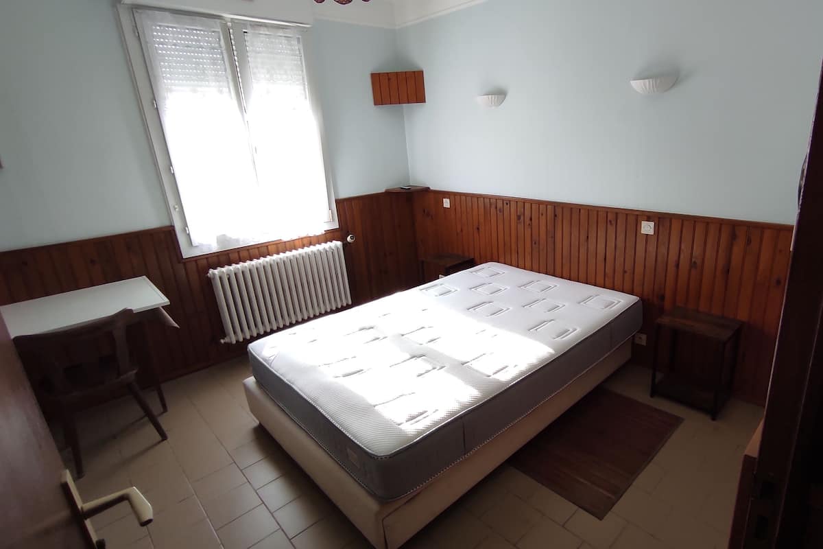 A room with a bed, a desk, a radiator, and a window.