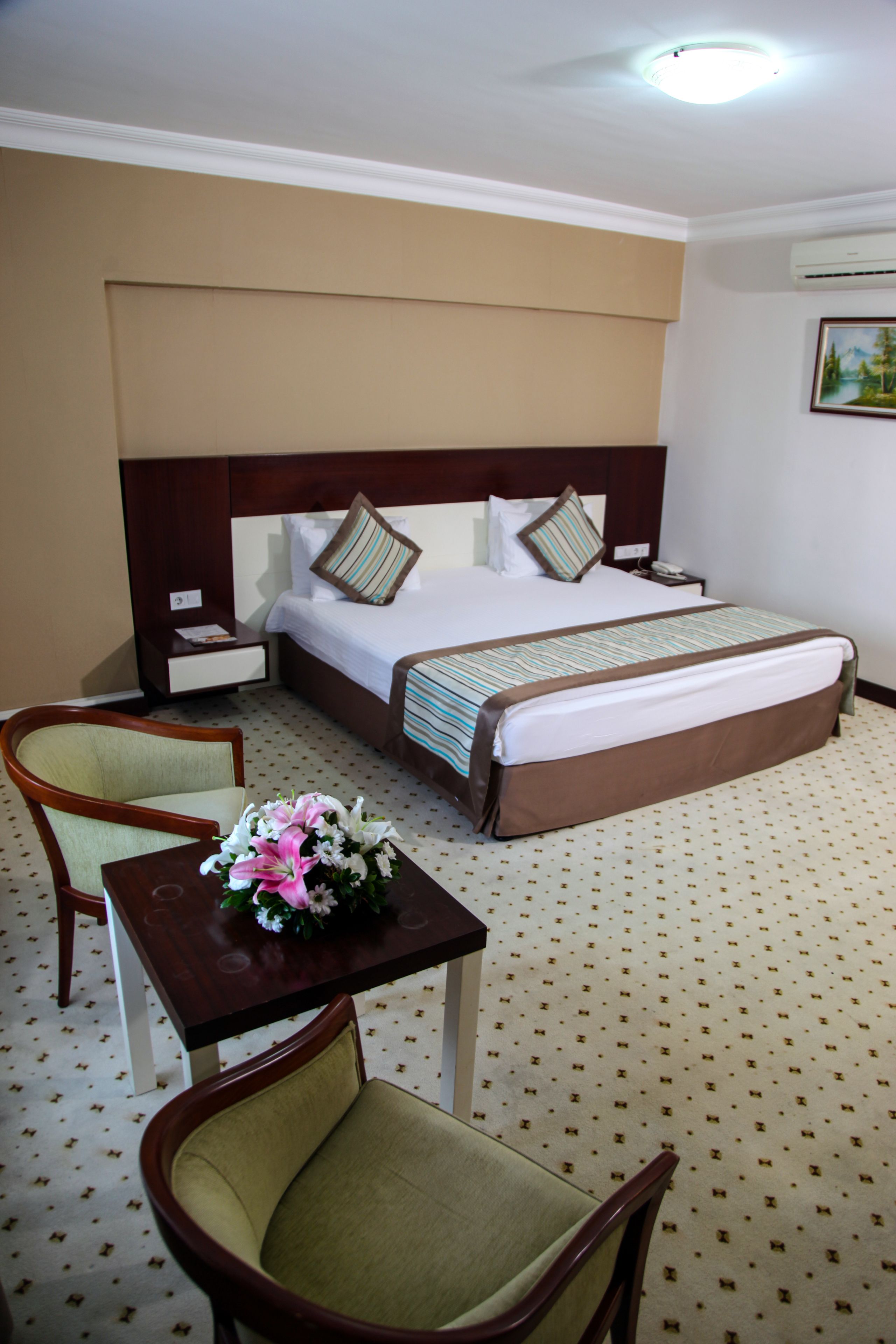 Habitación de hotel con cama, mesita de noche, escritorio con silla y un jarrón de flores.