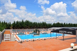 Un área de piscina en la azotea con sillones de descanso y sombrillas, rodeada de árboles.
