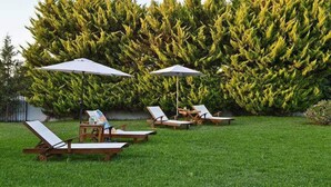 A garden with four wooden lounge chairs and two umbrellas, surrounded by a well-maintained hedge. - Villa Dimeon (West Achaea)