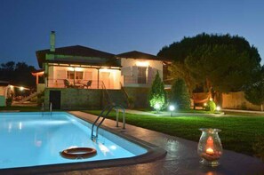 Une maison avec une piscine, un patio bien éclairé et un petit jardin.
