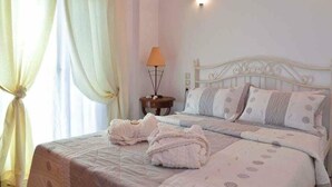 A bedroom with a bed, pillows, a lamp on a bedside table, and a window with curtains. - Villa Dimeon (West Achaea)