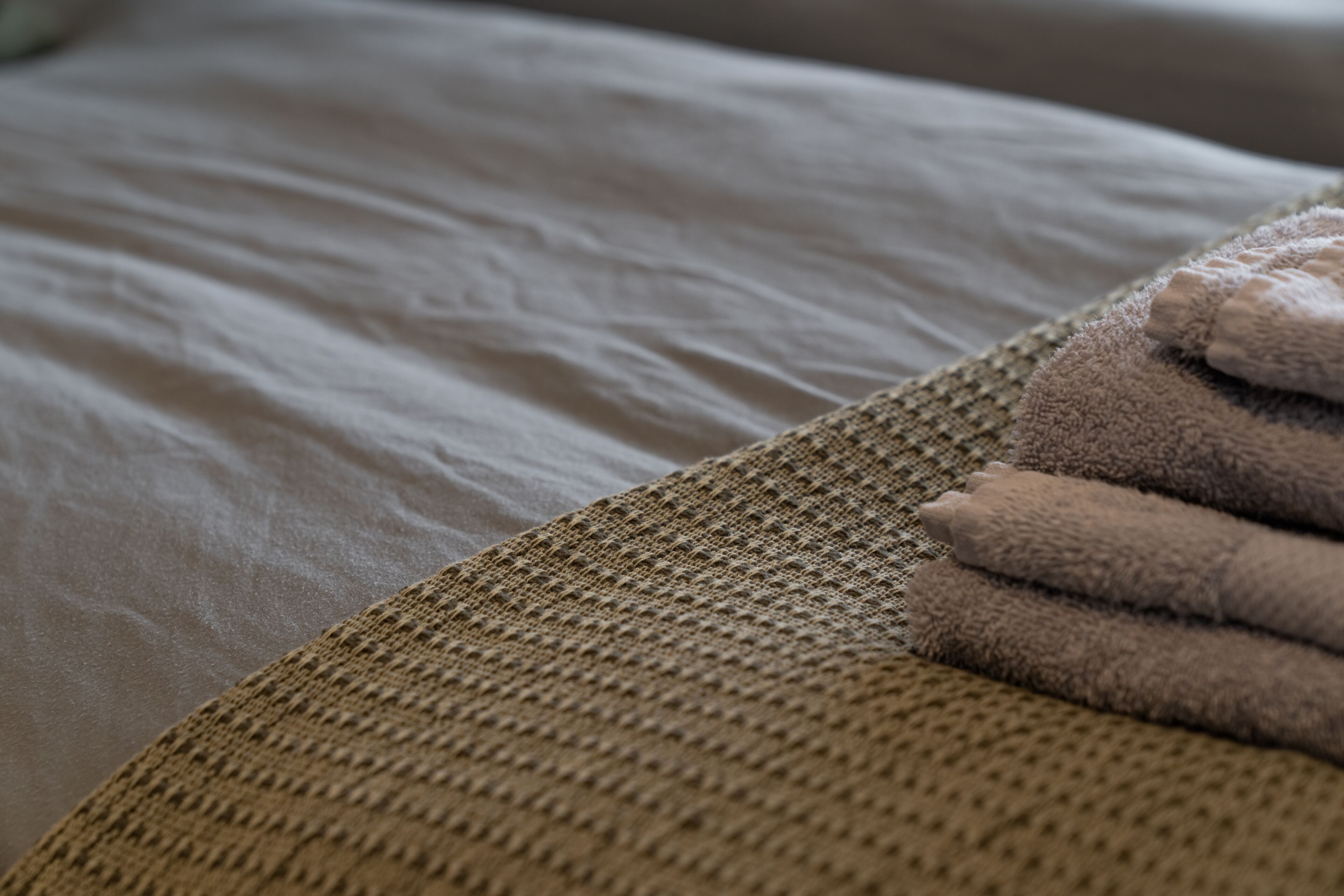 A bed with a textured beige blanket and a folded towel.
