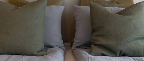 Una cama con múltiples almohadas en diferentes tonos de verde y gris.