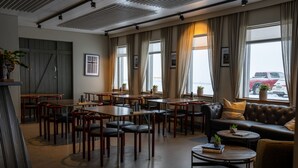 A spacious lounge area with multiple tables and chairs, a leather sofa, and large windows with curtains. -  Hotel Snaefellsnes - formally Hotel Rjukandi (Eyja- og Miklaholtshreppur)