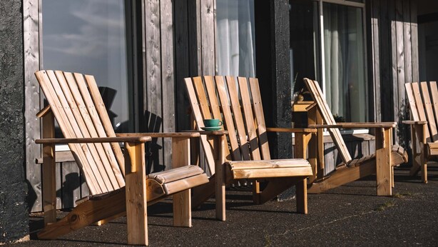 Wooden Adirondack chairs arranged outside a building with large windows. -  Hotel Snaefellsnes - formally Hotel Rjukandi (Eyja- og Miklaholtshreppur)