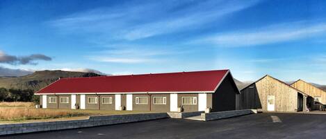 A building with a red roof and multiple windows, surrounded by a paved area and a grassy field.