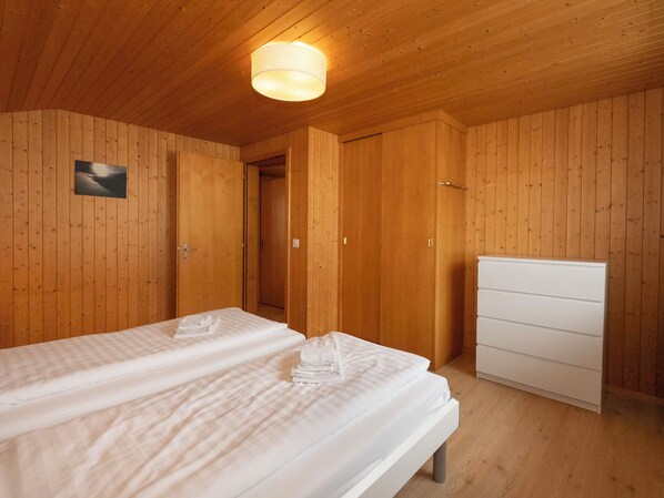 A wooden-paneled room with a bed, a dresser, and a door leading to another room.