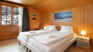 Ein Zimmer mit Doppelbett, Holzwänden, einem großen Fenster und Blick auf die Berge.