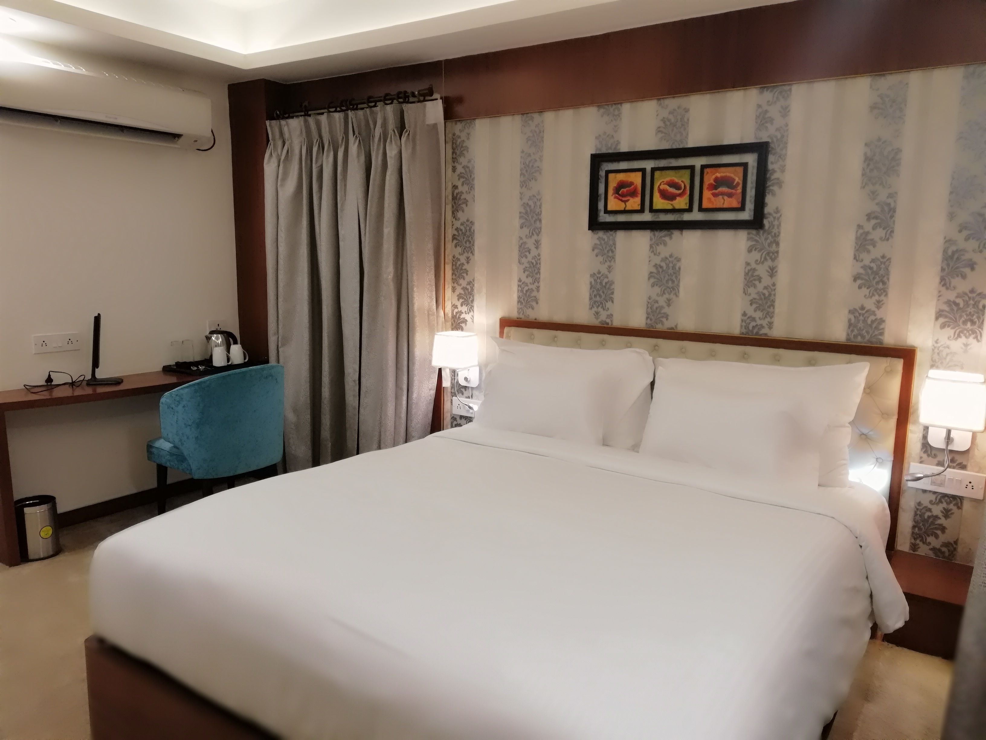 Une chambre d’hôtel avec un grand lit, un bureau avec une chaise, une lampe et un tableau au mur.