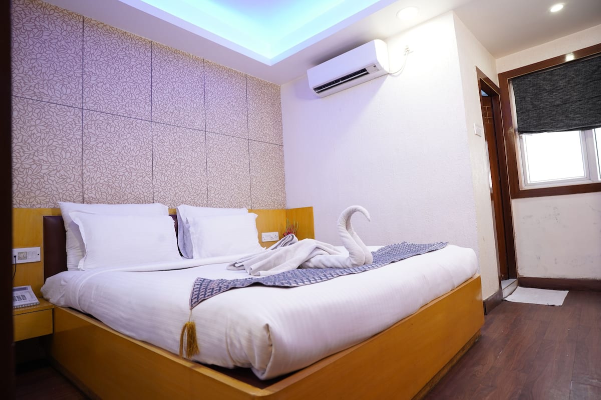 A neatly made bed with a swan towel arrangement, a bedside phone, and a wall-mounted air conditioner.
