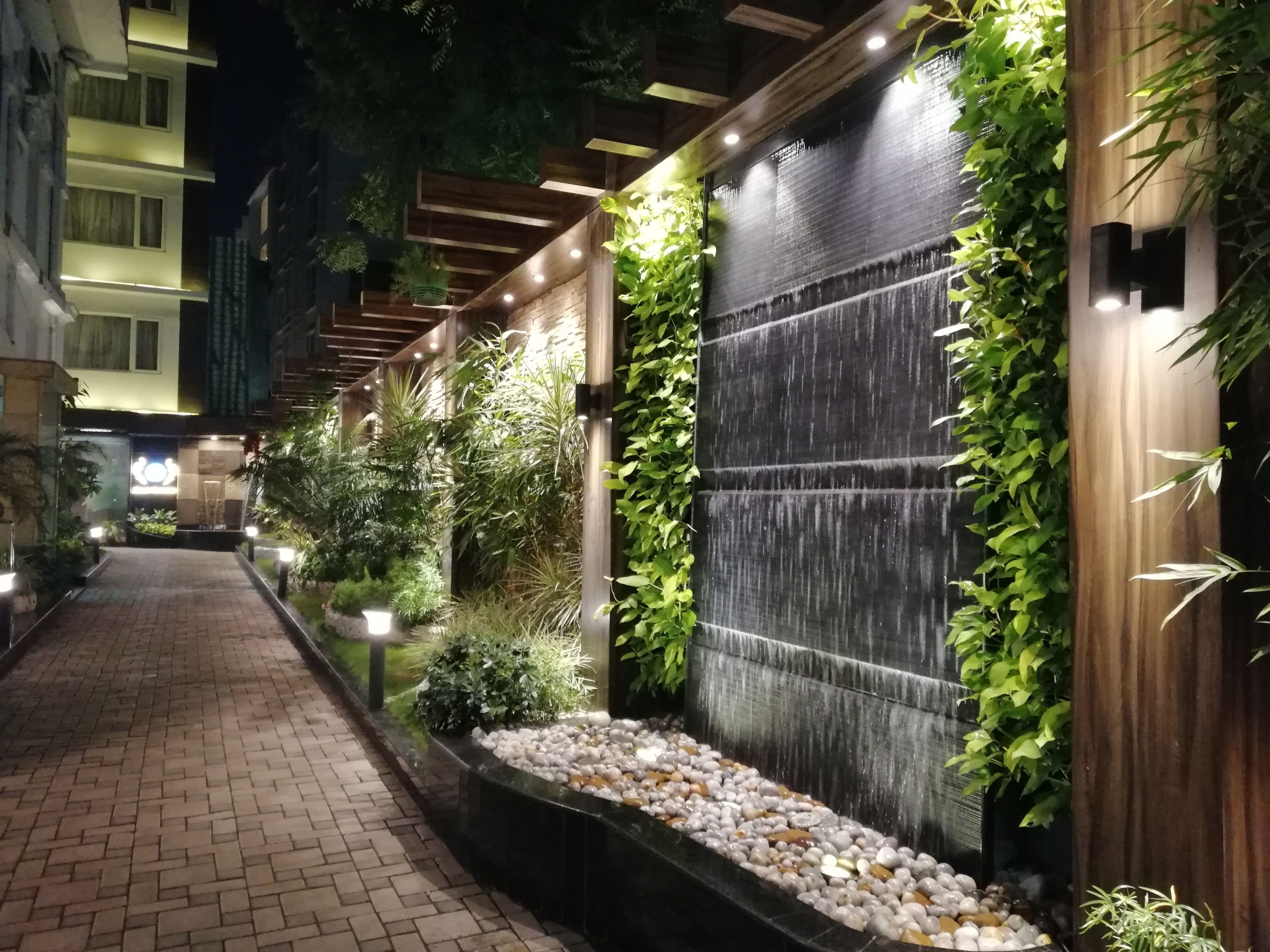 A nighttime walkway with a water feature, plants, and a brick path.