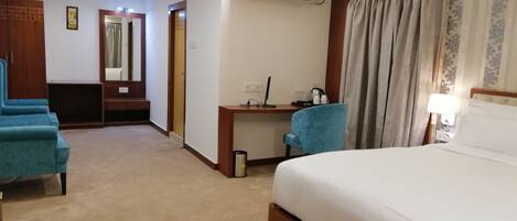 A hotel room with a large bed, a desk with a chair, a wardrobe, and a ceiling fan.