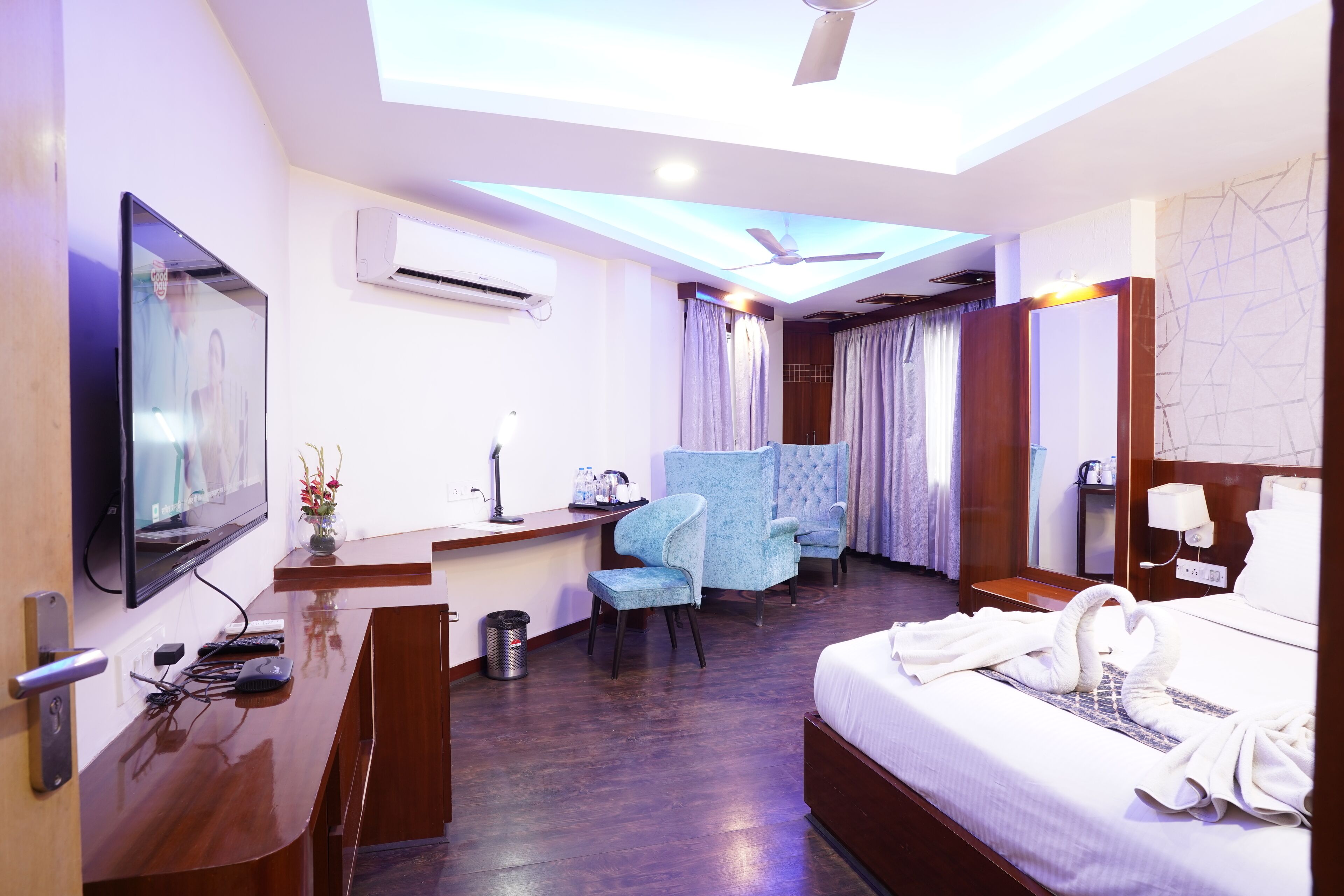 A hotel room with a bed, a desk, a chair, a TV, an air conditioner, and a ceiling fan.