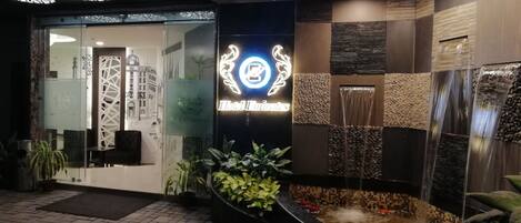 A hotel entrance with a modern design, featuring a neon sign, a water feature, and a brick-paved entrance.