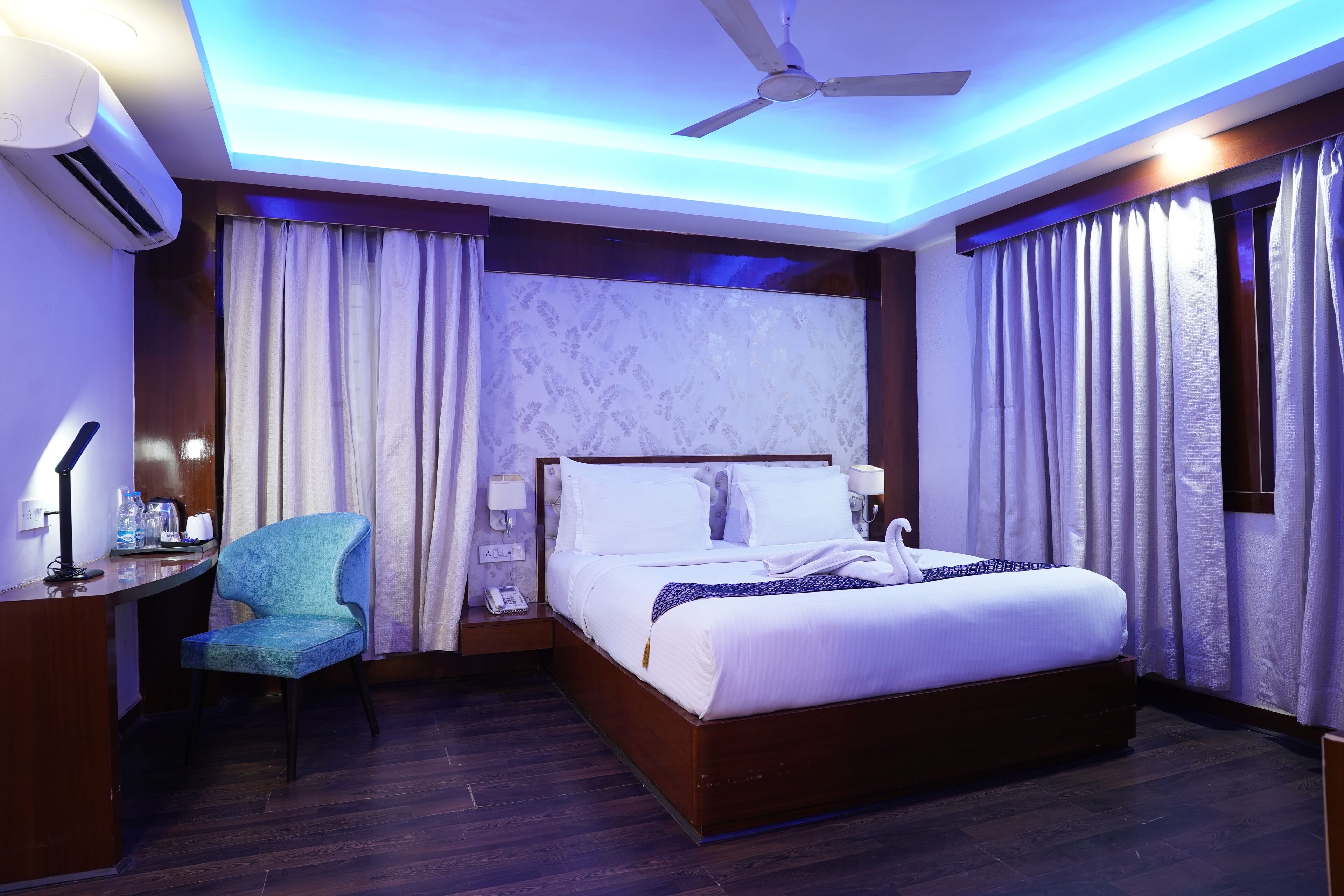 A modern hotel room with a large bed, a desk, a chair, and a ceiling fan.