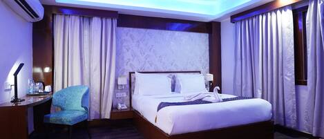 A modern hotel room with a large bed, a desk, a chair, and a ceiling fan.
