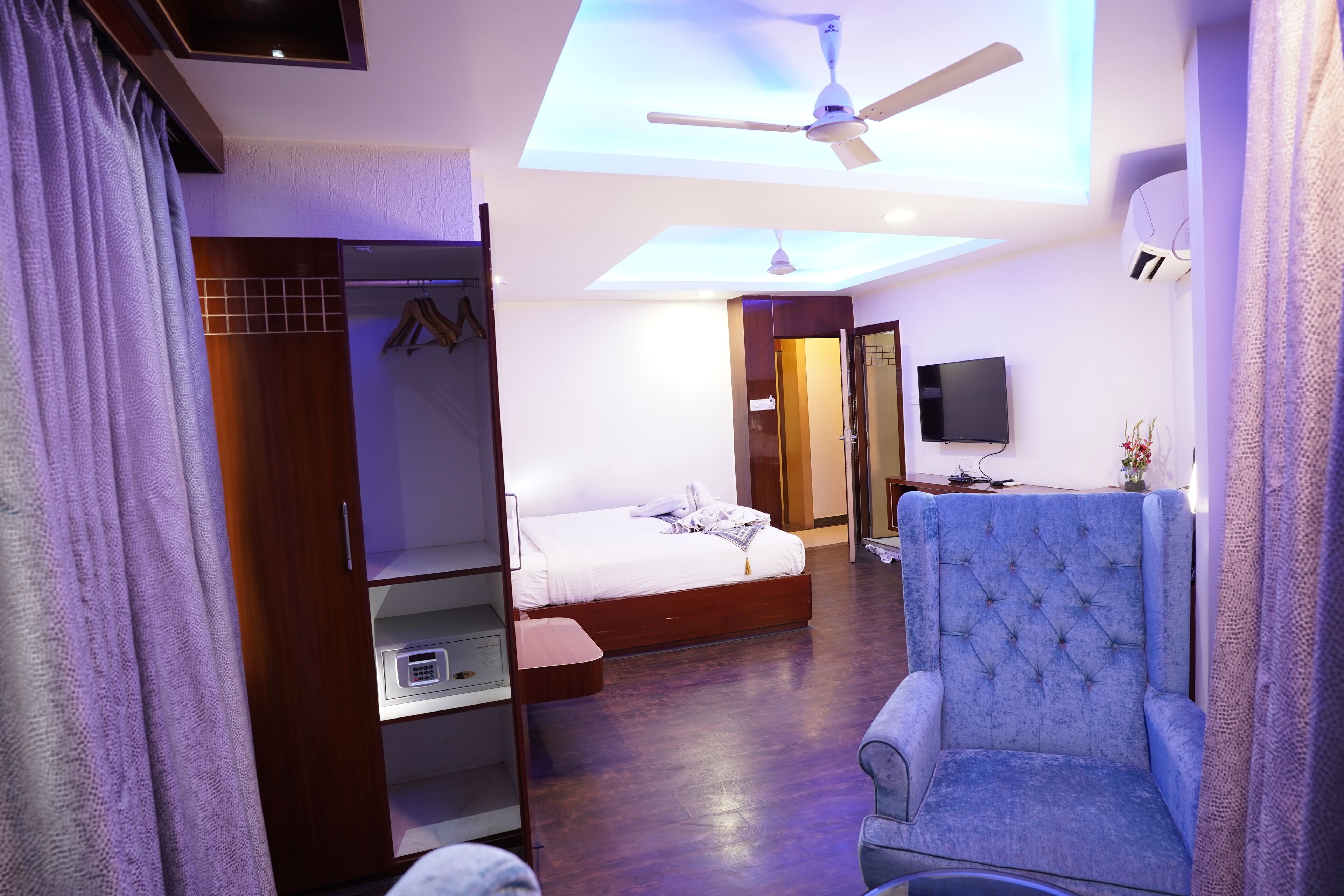A modern bedroom with a large bed, a seating area, and a ceiling fan.