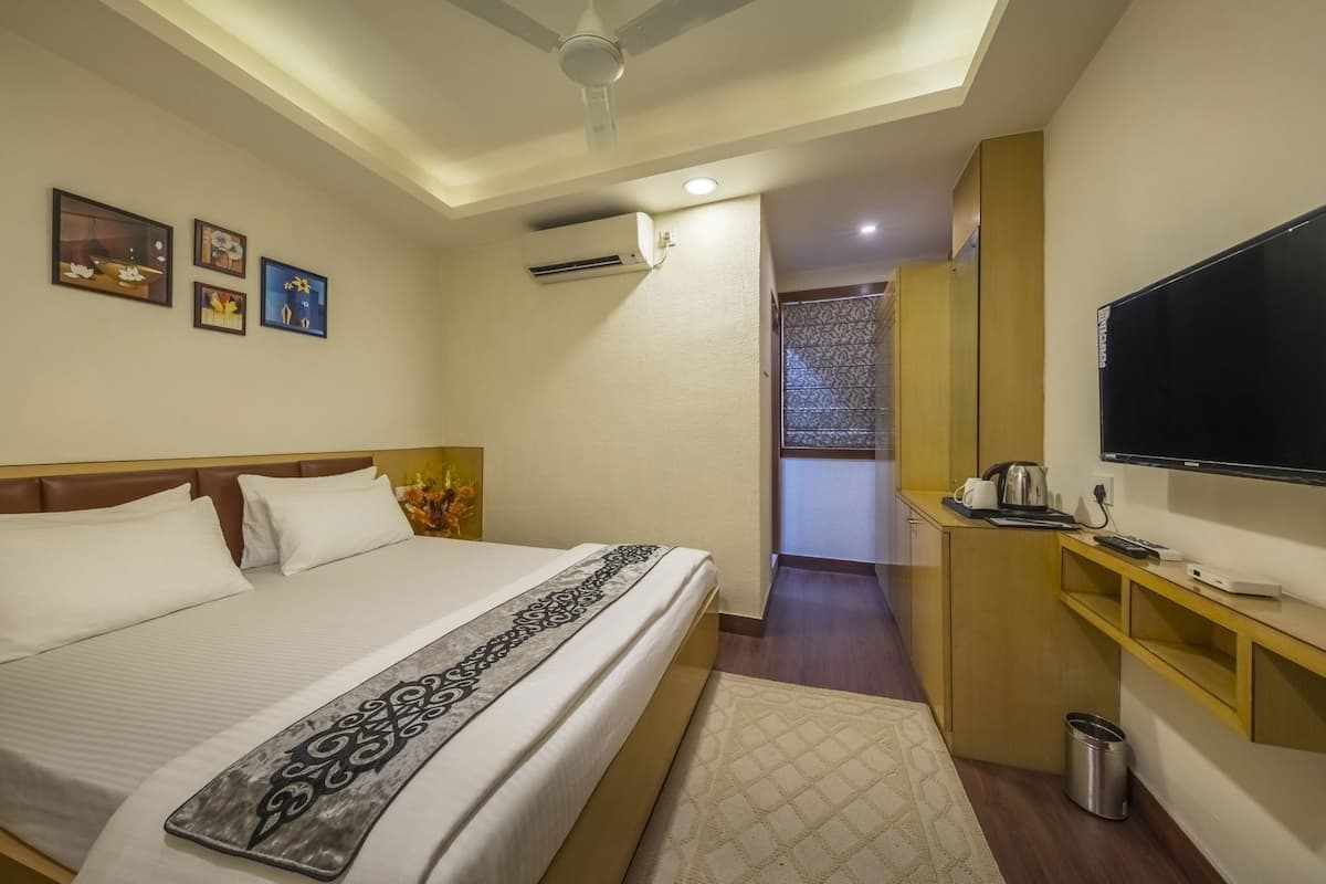 A hotel room with a bed, a television, a desk, and a small kitchenette.