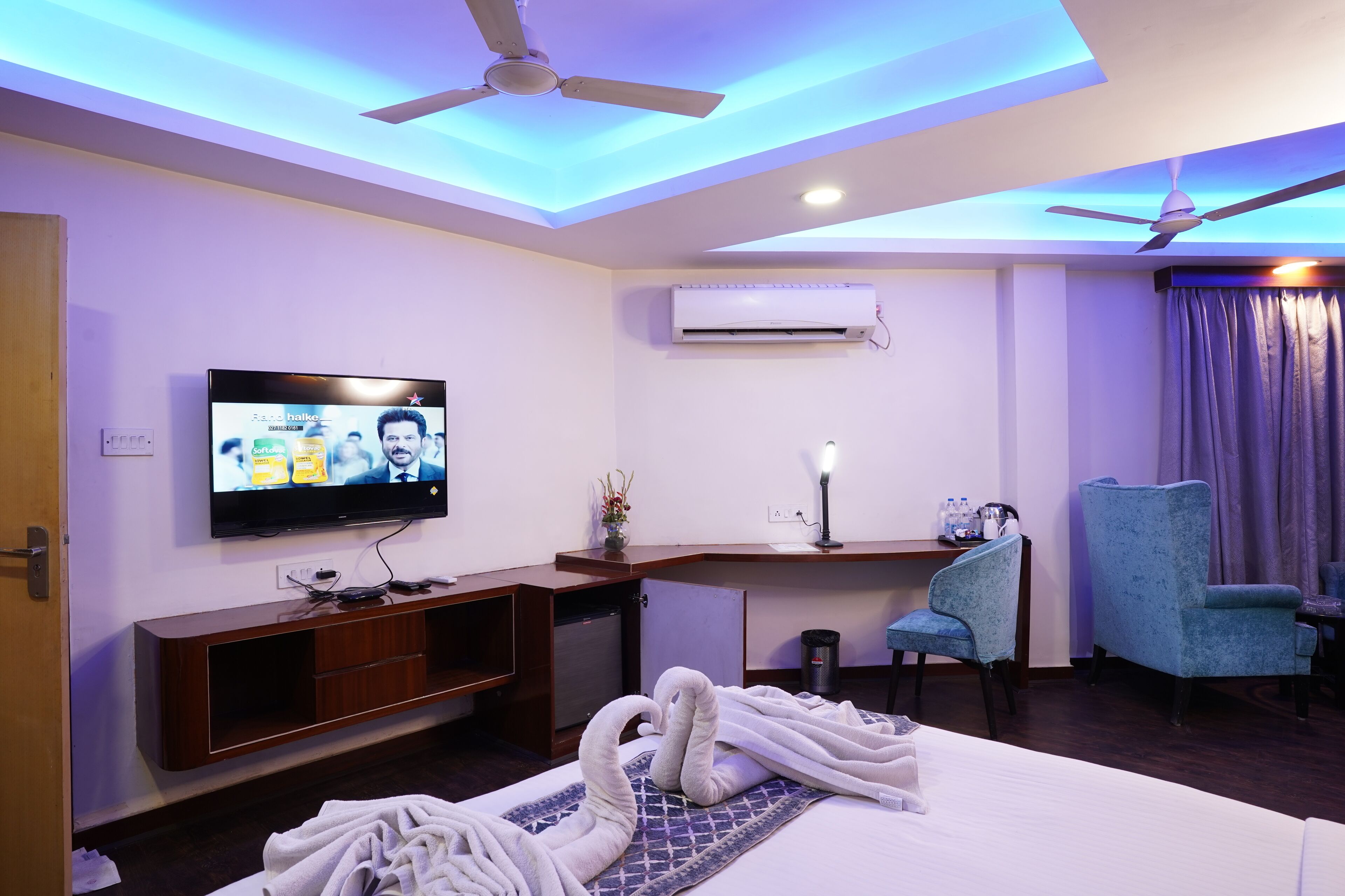 A hotel room with a bed, a desk, a television, a ceiling fan, and a window with curtains.