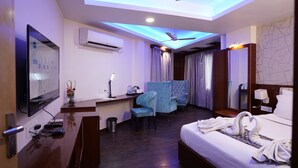Habitación de hotel con cama, escritorio, silla, televisor y ventilador de techo.