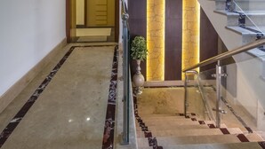 Un moderno vestíbulo de hotel con suelo de mármol, una escalera con barandillas de vidrio y una puerta con la indicación '301'.
