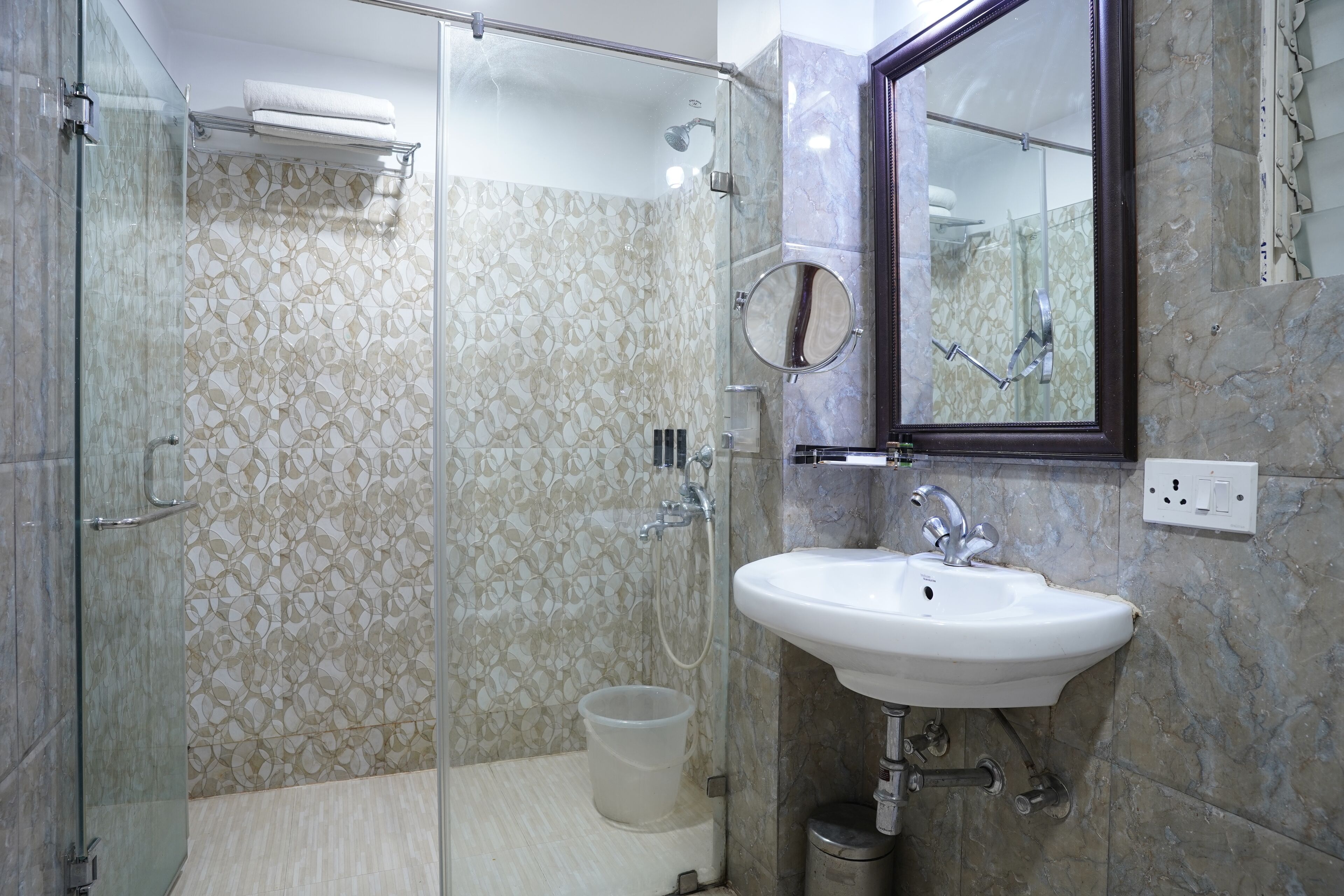 Ein modernes Badezimmer mit einer gläsernen Duschkabine, einem weißen Waschbecken und einer Wand mit Marmoroptik.