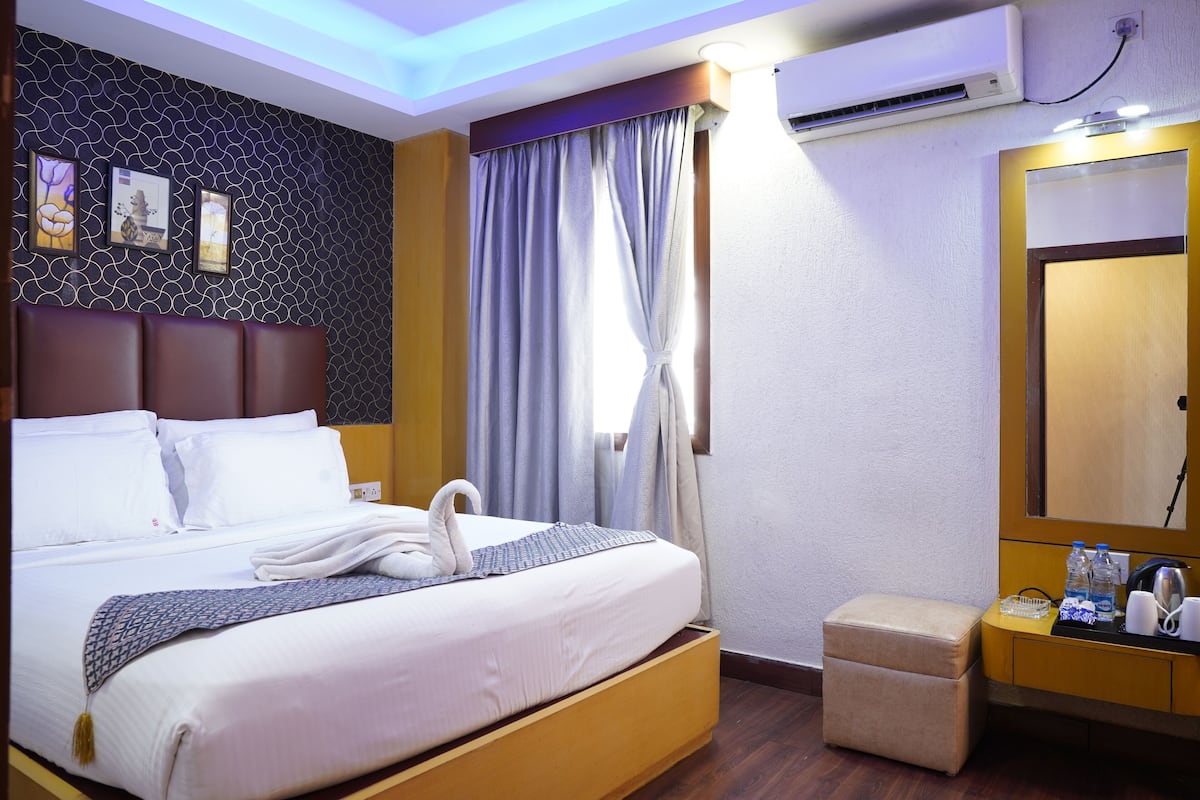 A hotel room with a bed, a bedside table with a lamp, a mirror, and a window with curtains.
