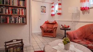 Ein gemütliches Wohnzimmer mit Bücherregal, einem roten Sessel, einer Couch und einem Couchtisch mit Pflanze.