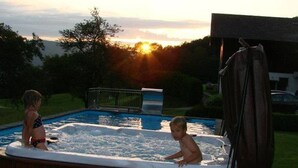 Een jacuzzi met twee personen, omgeven door gras en bomen.