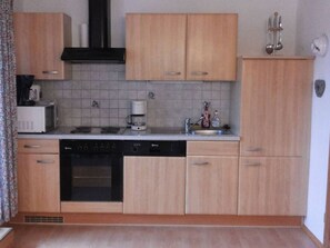 Een keuken met houten kastjes, een vaatwasser, een oven, een koffiezetapparaat en een spoelbak.