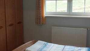 Een kamer met een houten hoofdbord, een raam met gordijnen, een radiator en een bed met een beddeken met een patroon.