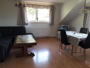 Et værelse med et træspisebord, en sort sofa, et lille fjernsyn og et vindue med gardiner.