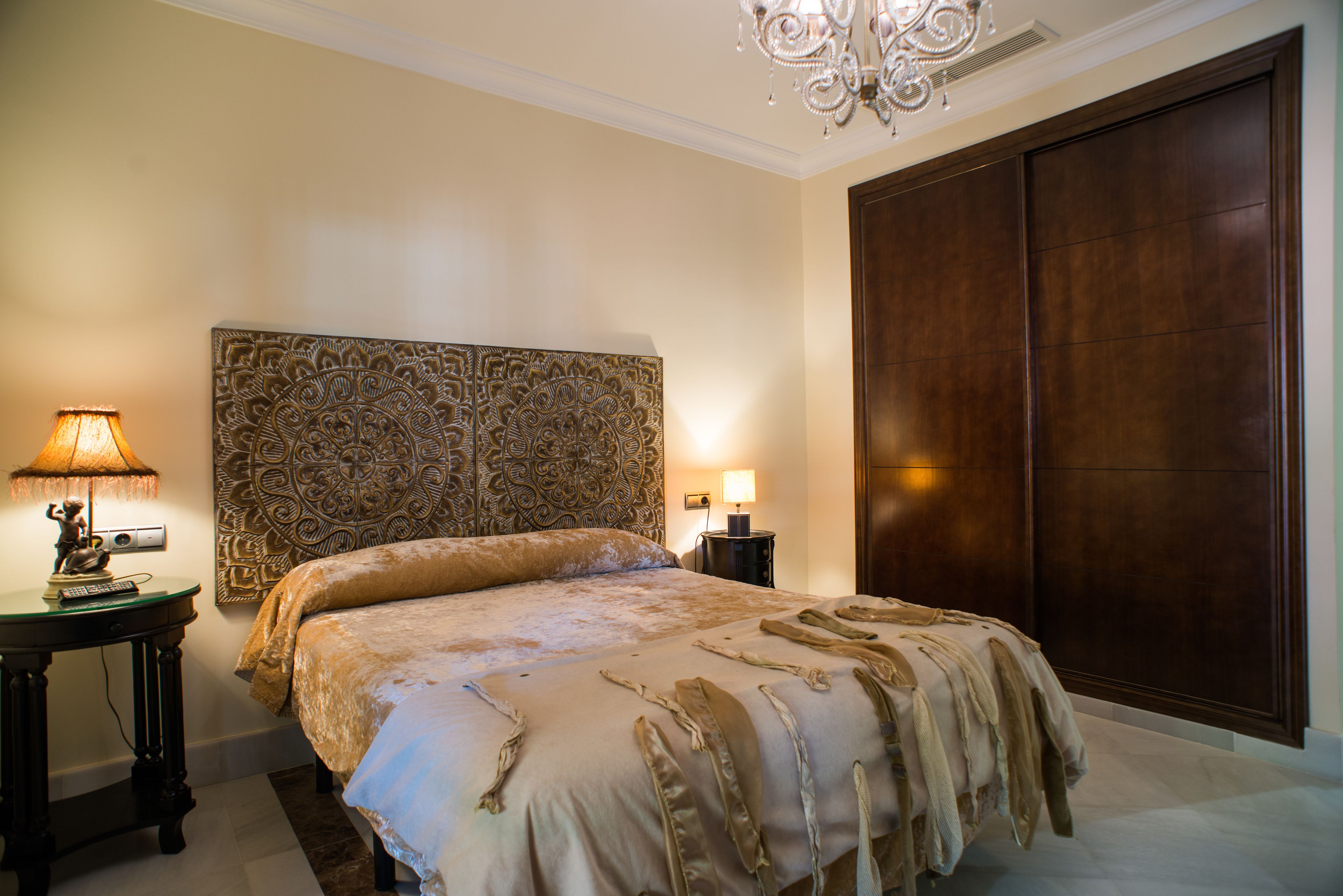 Un dormitorio con una cama grande, un cabecero decorativo, una mesita de noche con lámpara y un armario.