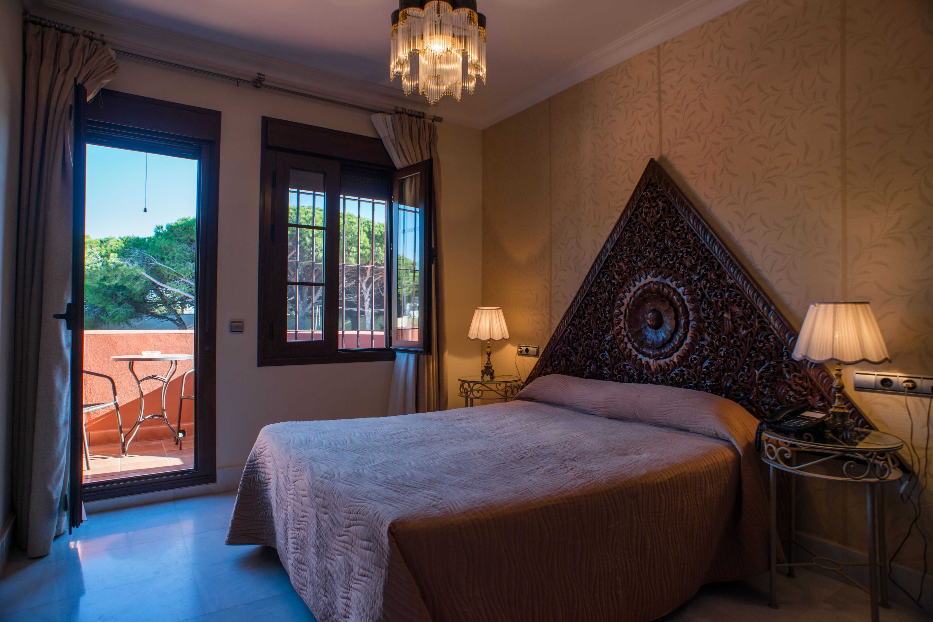 A bedroom with a large bed, a chandelier, and a view of the outdoors through a sliding door.