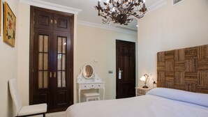 A bedroom with a large bed, a wooden headboard, a white dresser, a chair, and a chandelier. - Hotel Coral Playa (Chiclana de la Frontera)