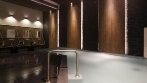 Une salle de bain moderne dotée d’un plancher chauffant, d’un jacuzzi entouré de parois de verre et d’une rangée de lavabos avec des miroirs.