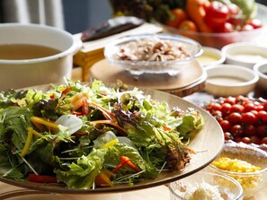 A table with a variety of food items including a salad, tomatoes, and bowls of dressing.