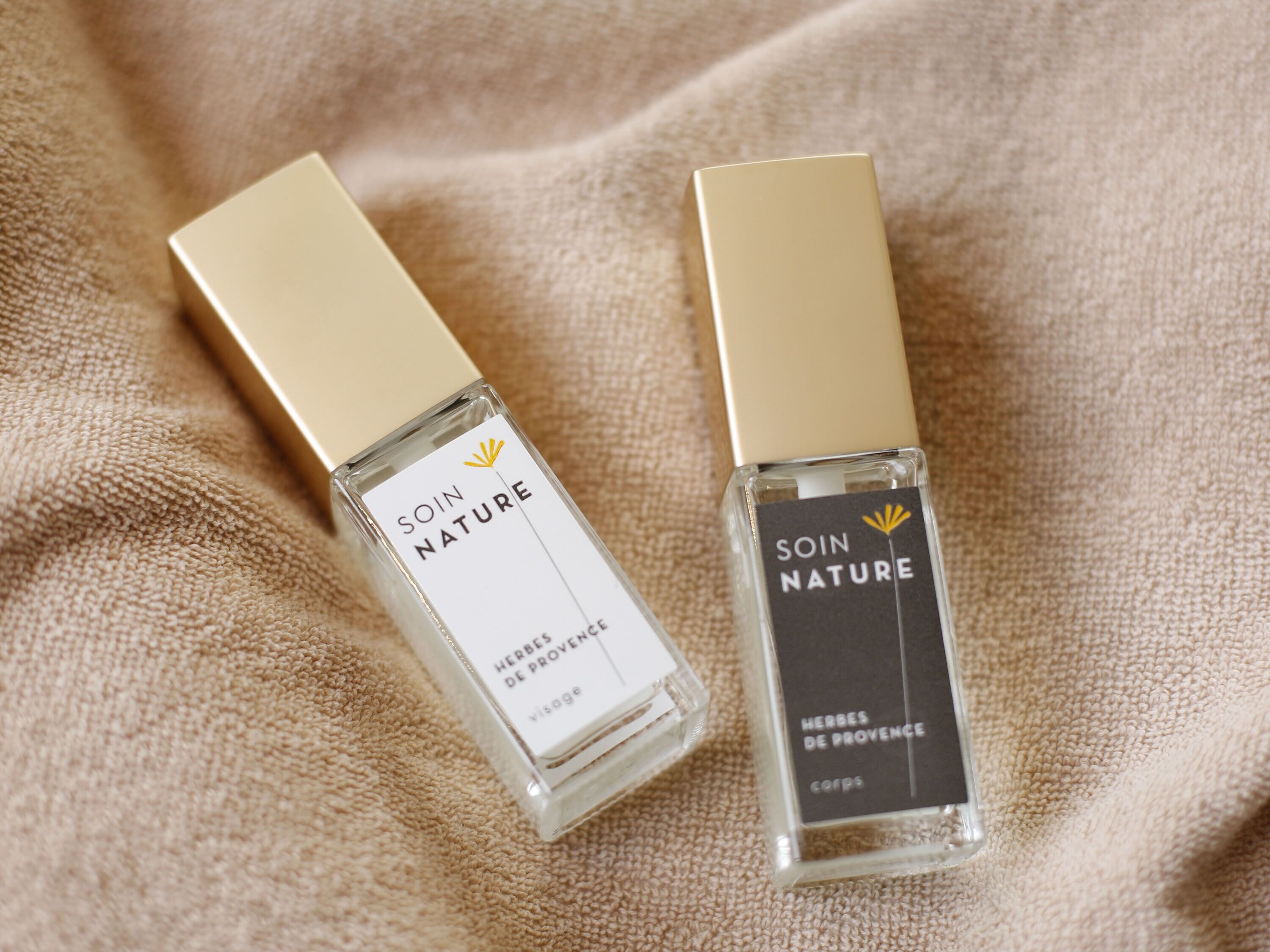 Twee flesjes 'Soin Nature' eau de cologne met gouden dopjes op een geribbelde beige stof.