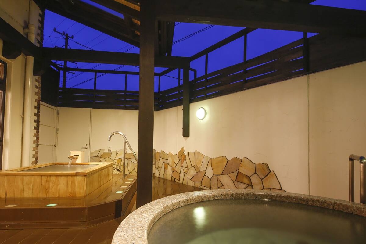 A spa area with a hot tub, wooden flooring, stone wall, and a ceiling with a skylight.
