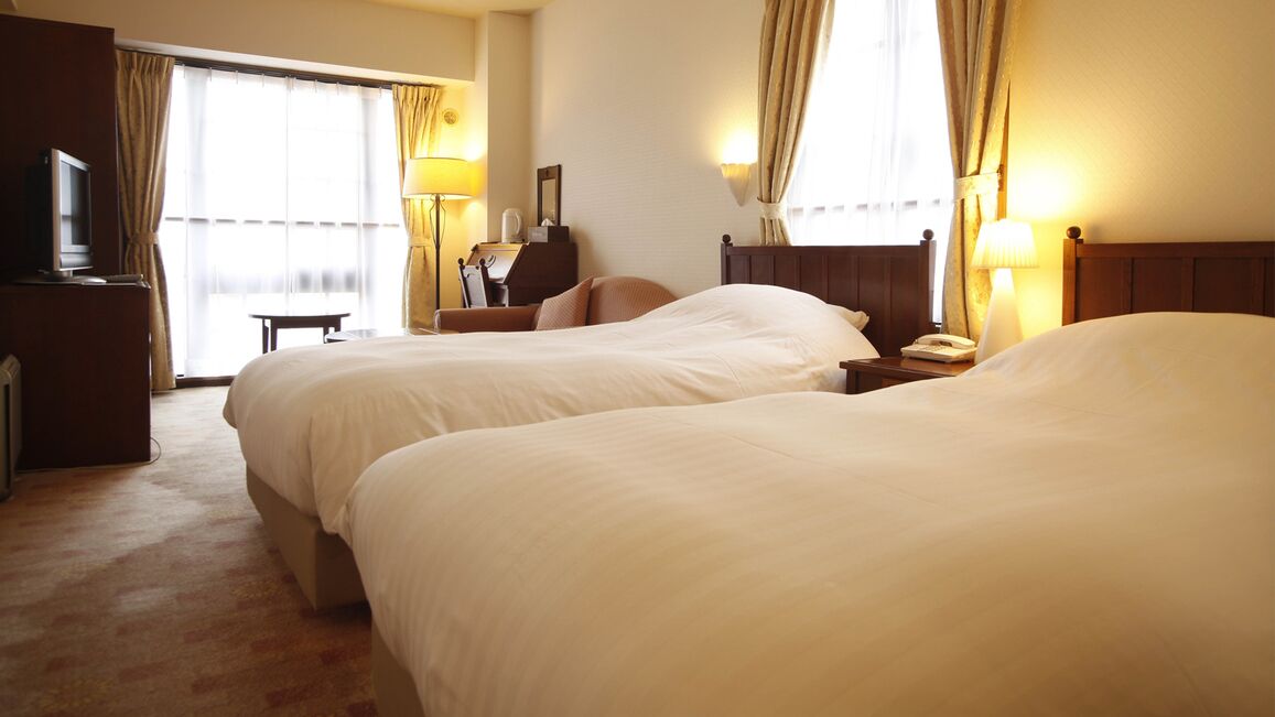 Een hotelkamer met twee bedden, een bureau, een televisie en een raam met gordijnen.