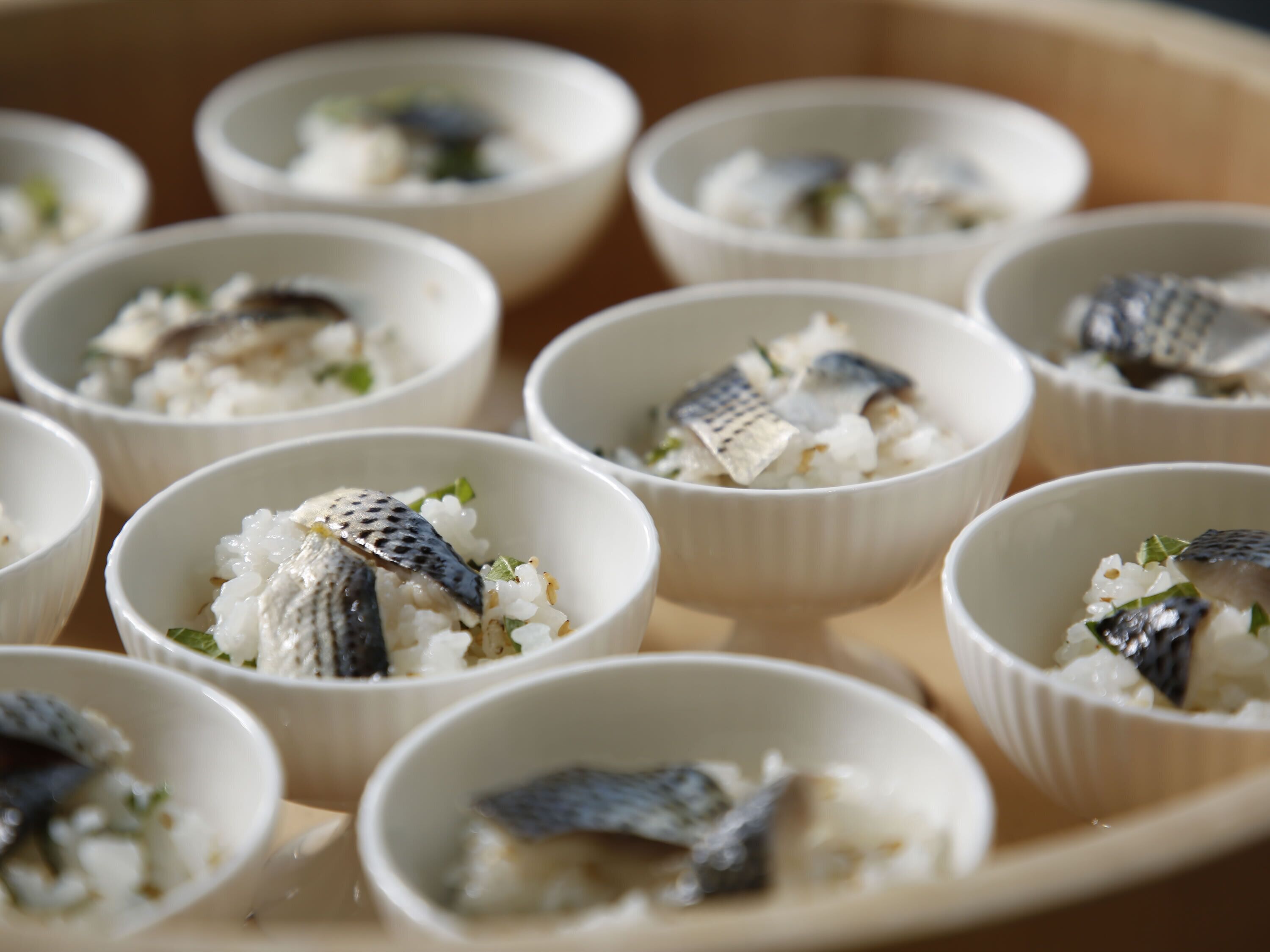 Mehrere Schüsseln Reis mit Fisch und grünen Kräutern.