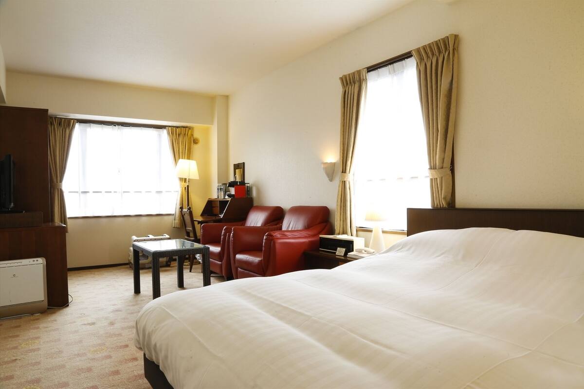 A hotel room with a large bed, a desk, a chair, and a television.