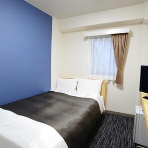 Een hotelkamer met een bed, een televisie, een raam met gordijnen en een bureau.